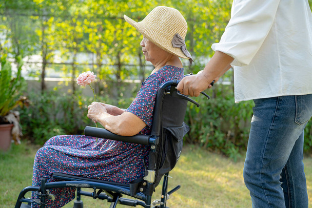 Опекун помощь и уход азиатских пожилых или пожилых пожилая женщина пациентка сидя и счастливый на инвалидной коляске в парке, здоровый сильный медицинский концепт. - Фото, изображение