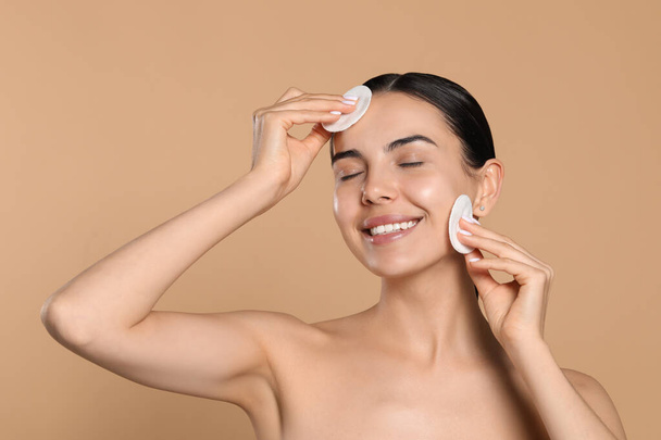 Young woman using cotton pads with micellar water on beige background - Фото, зображення