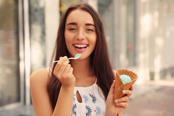 Happy young woman with delicious ice cream in waffle cone outdoors - Фото, зображення