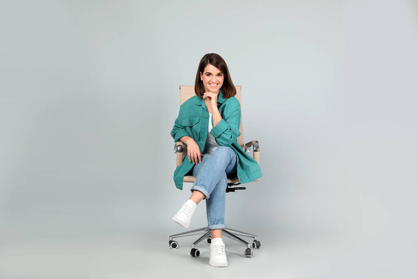 Young woman sitting in comfortable office chair on grey background - Photo, Image