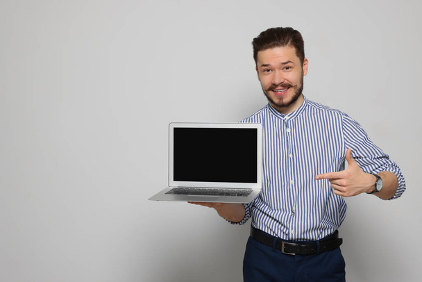 Emotional man pointing at laptop on light grey background. Space for text - Foto, imagen