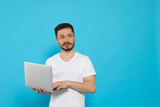Pensive man using laptop on light blue background. Space for text - Φωτογραφία, εικόνα