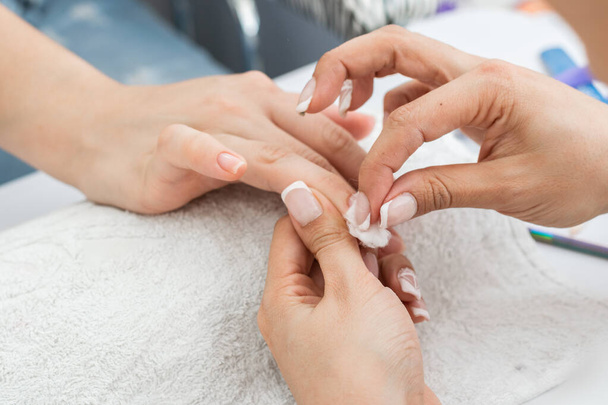 latina manicurist performing a proper nail cleaning with a cotton swab, removing excess moisture and liquid on the nail. woman learning how to clean nails. - Photo, Image