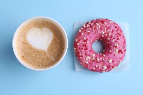 Tasty frosted donut and cup of coffee on light blue background, flat lay - Fotó, kép