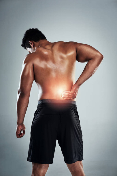 You can hurt your back if you go too heavy. Rearview shot of a sporty young man holding his back in pain against a grey background - Foto, Bild