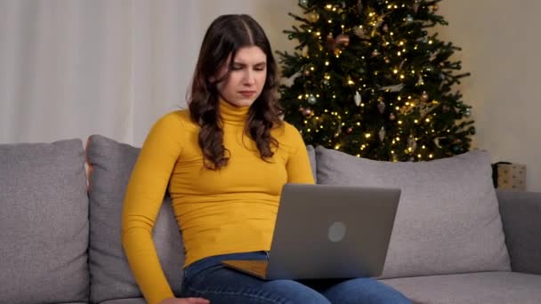 Angry businesswoman looks at laptop screen display upset about problem of gifts for New Year. Stressed woman read bad online news on computer on background Christmas tree at cozy home - Séquence, vidéo