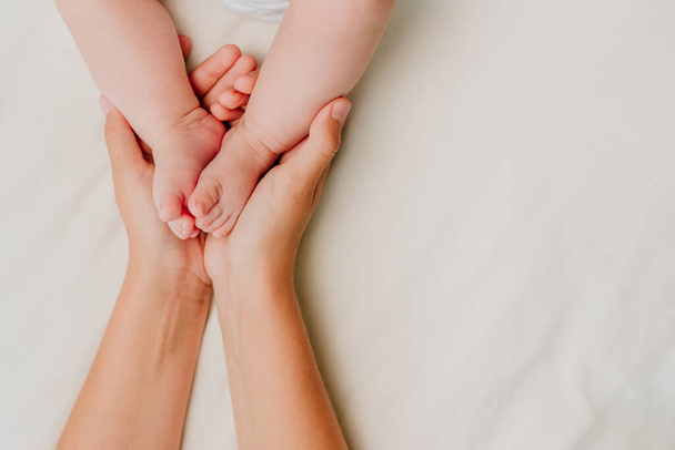 Felnőtt kéz tartja újszülött baba lábát fehér textil háttér üres hely szöveges. Felülnézet, lapos fektetés. - Fotó, kép