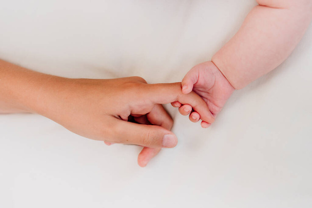 Main du nouveau-né tenant le doigt d'un adulte sur fond textile blanc avec espace vide pour le texte. Vue de dessus, plan plat. - Photo, image