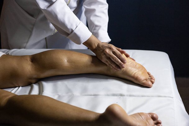 A professional doing therapeutic massage on the foot of the patient who is lying on the stretcher. - Foto, Imagen
