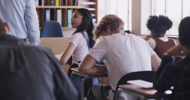 School teacher helping a girl student writing a book test, learning or exam in a teaching classroom. High school students studying and working for knowledge, education and development at their desks. - Filmagem, Vídeo