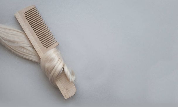 Top view of a wooden comb in curls of delicate blond blonde hair. - Fotó, kép