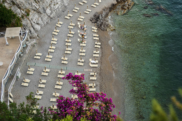 Отдых на юге Италии. Береговая линия с шезлонгами и зонтиками у моря под скалой. Зоны отдыха, пляжные комплексы - Фото, изображение