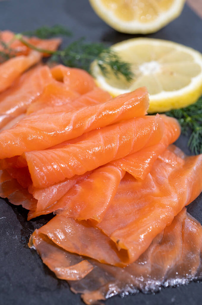 Slices of tasty smoked Scottish salmon fish served on black plate with lemon and fresh dill close up - Foto, immagini