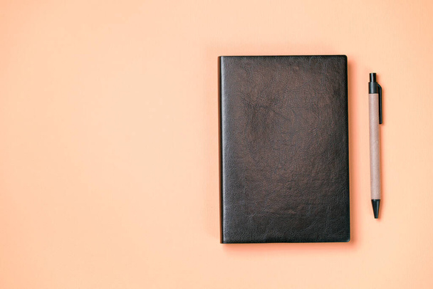 Czarny skórzany notatnik na papierowym pomarańczowym tle, makieta notatnika, zdjęcie z góry - Zdjęcie, obraz