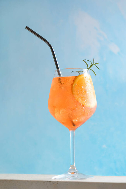 Classic italian aperitif aperol spritz cocktail in glass with ice cubes and slice of orange with light blue background on marble stone table, traditional summer fresh iced drink, close up - Fotó, kép