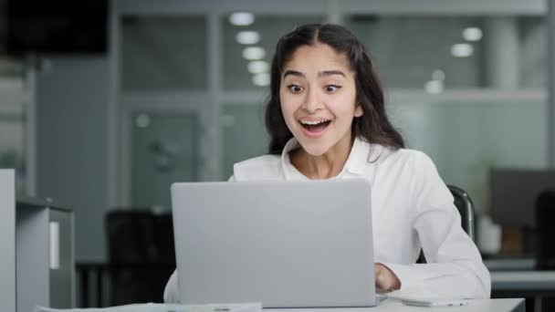 Young woman manager sitting in office looking at laptop screen receiving notification reads good news rejoices in success celebrating victory feels good luck receives promotion at work gets job bonus - Video, Çekim