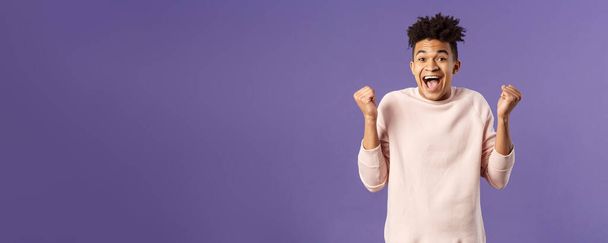 Portrait of happy, cheerful triumphing young hipster guy with dreads, dancing like champion, celebrating success or victory, passed test, fist pump smiling and rejoicing, purple background. - Photo, Image