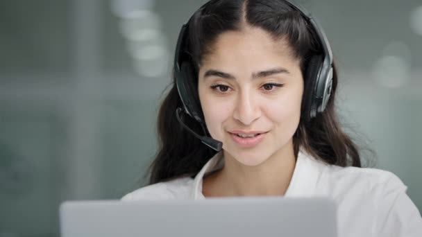 Close-up young woman assistant sales agent advisor hotline consultant answering incoming call using headset looking at laptop screen talking to client giving professional support advertises services - Video, Çekim