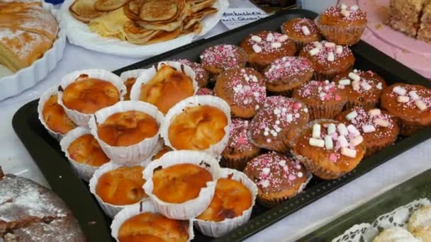 Σπιτικά κέικ, φρεσκοψημένα cupcakes με ζαχαρωτά στην αγορά. Η επιγραφή στα γερμανικά ονόματα αρτοσκευασμάτων. - Πλάνα, βίντεο
