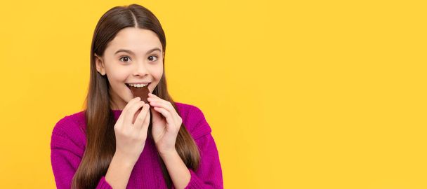 Happy girl child bite tasty chocolate slab yellow background, sweet-tooth. Horizontal poster of isolated child face, banner header, copy space - Foto, afbeelding