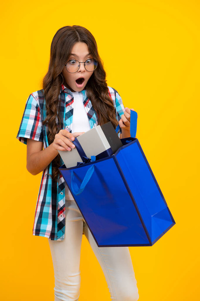 Дитяча дівчина тримає торгову сумку, насолоджуючись продажем ізольовано на жовтому тлі. Портрет дівчини-підлітка готовий йти за покупками. шокована здивована дівчина-підліток
 - Фото, зображення