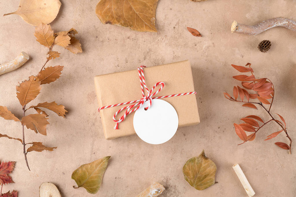 Autumn background: fallen leaves, dry plants with handmade gifts wrapped in craft paper and rope with gift tag mockup on natural beige background. Thanksgiving autumnal background, top view, flat lay - Foto, Bild