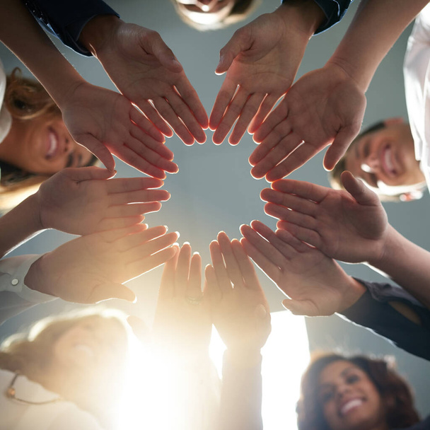 Unity is key to accomplishing greatness. Low angle shot of a group of businesspeople joining their hands together in unity - 写真・画像