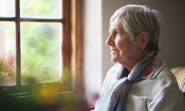 Ευτυχισμένη ηλικιωμένη γυναίκα που κοιτάζει έξω από το παράθυρο σκεπτόμενη αναμνήσεις συνταξιούχος συνταξιούχος έννοια τρόπου ζωής. - Φωτογραφία, εικόνα