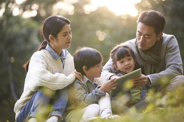 都会の公園でリラックスしている2人の子供を持つアジア系の家族 - 写真・画像