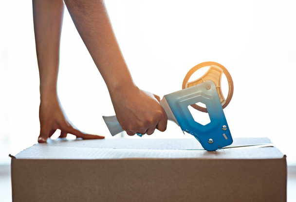 Moving is easy when you have the right tools. an unrecognizable young woman closing a cardboard box with tape at home - Foto, Imagen