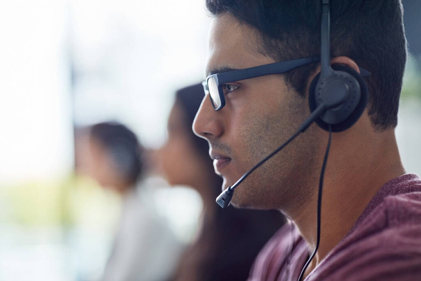 Im focused on helping each customer best I can. a young man wearing a headset with his colleagues blurred in the background - Foto, Imagem