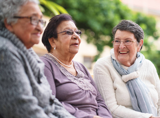 Happy elderly women sitting on bench in park smiling best friends enjoying retirement together. - Foto, imagen