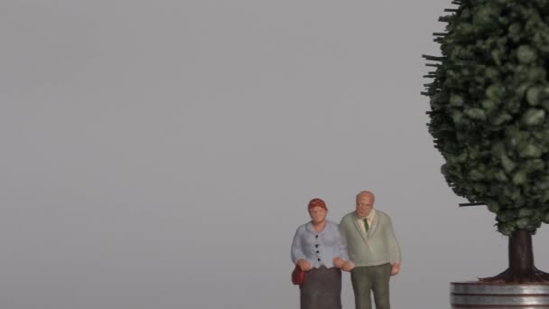 Miniature people and the concept of an aging society. A miniature old couple standing next to a pile of step coins. - Imágenes, Vídeo