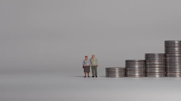 Miniature people and the concept of an aging society. A miniature old couple standing next to a pile of step coins. - Filmagem, Vídeo