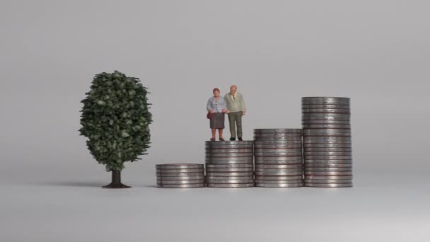 Miniature people and the concept of an aging society. A miniature old couple standing on a pile of step coins. - Filmagem, Vídeo