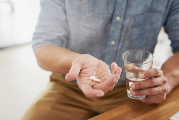 Taking his prescribed treatment. Closeup shot of an unrecognisable man holding a glass of water and medication in his hands - Foto, immagini