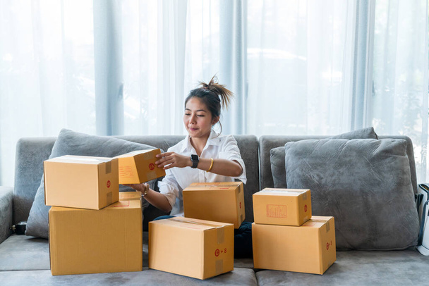Beautiful Asian women sitting on sofa with many parcel box with small businesses sell to customer on shopping online. Concept selling and shopping online from home - Photo, Image