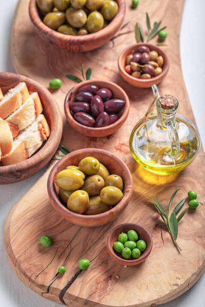 Healthy olives and extra virgin olive oil as Italian appetizer. Set of green and black olives in wooden bowls. - Фото, изображение