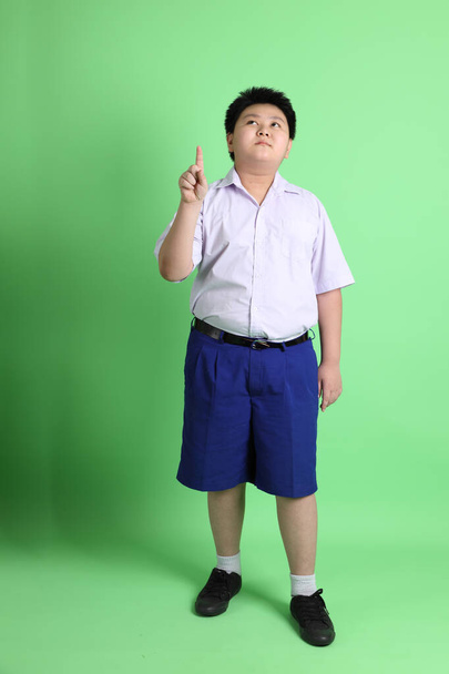 Der asiatische Junge mit Studentenuniform auf grünem Hintergrund. - Foto, Bild