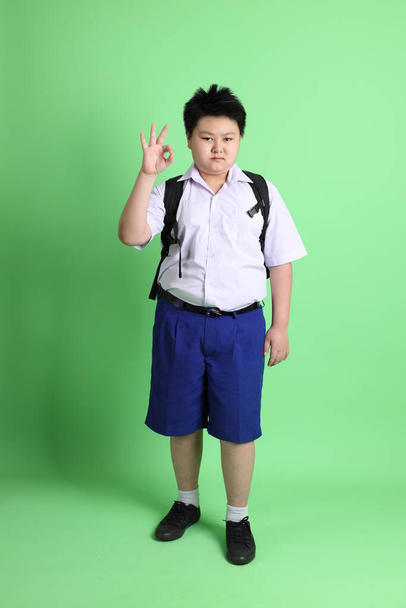 Der asiatische Junge mit Studentenuniform auf grünem Hintergrund. - Foto, Bild