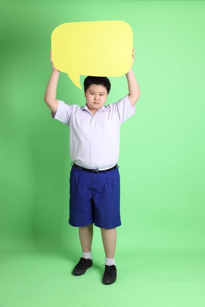 Az ázsiai fiú diákegyenruhában a zöld háttéren. - Fotó, kép