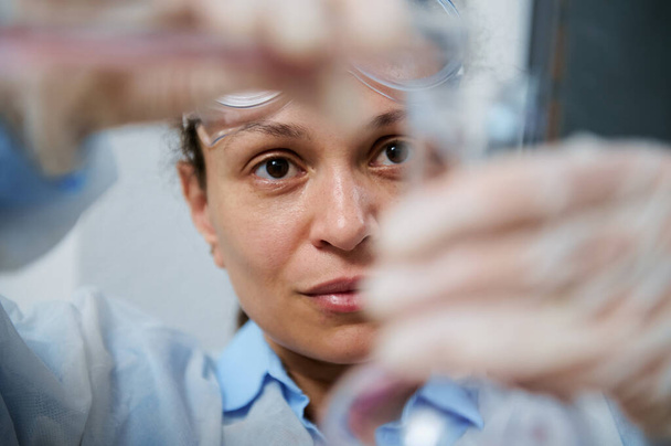 Εστίαση σε γυναικείο εργαστηριακό προσωπικό, χύνοντας ροζ υγρή χημική ουσία από γυάλινη φιάλη μέσω χοάνης σε δοκιμαστικό σωλήνα, κατά τη διεξαγωγή αναλύσεων σε ιατρικό εργαστήριο - Φωτογραφία, εικόνα