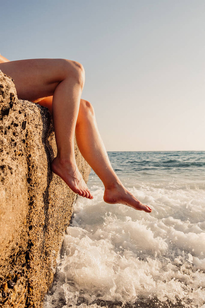 Young woman legs resting on a rock in the sea waves on vacation on the seaside - Foto, Imagem