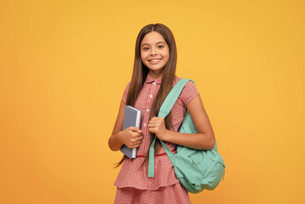 Ευτυχισμένο παιδί με βιβλίο εργασίας σε κίτρινο φόντο. Σεπτέμβριος 1. Ευτυχισμένη παιδική ηλικία. Παιδί με σχολική τσάντα. Έφηβη κουβαλάει σακίδιο. Πίσω στο σχολείο. Ημέρα γνώσης. έννοια της εκπαίδευσης. - Φωτογραφία, εικόνα