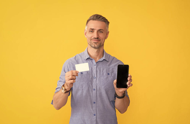 man pay in online banking. shopping app. cyber monday. fast payment. smiling guy show smartphone. customer using online money on mobile phone. show business name card. credit or debit card. - Photo, Image