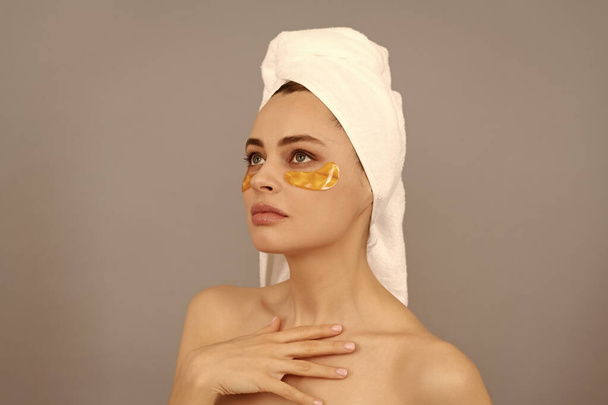 jonge vrouw met badstof handdoek gebruik gezicht gouden ooglapje voor de huid, huid. - Foto, afbeelding