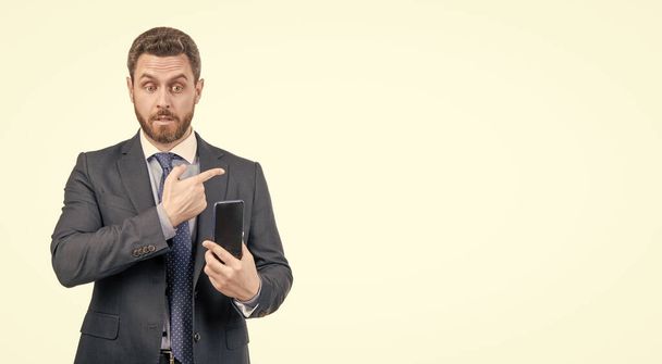 Профессиональный бизнесмен в формальном костюме держит мобильный телефон, указывая пальцем на пространство для копирования, изолированное на белом, реклама. - Фото, изображение