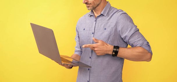 περικοπή άνθρωπος δείχνοντας δάχτυλο στον υπολογιστή σε κίτρινο φόντο, επιχείρηση σε απευθείας σύνδεση. - Φωτογραφία, εικόνα