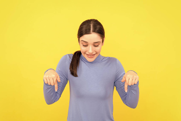 woman portrait pointing fingers down on copy space yellow background, presenting, - Fotoğraf, Görsel
