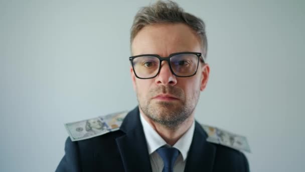 Formally dressed man with glasses made his shoulder straps out of US dollar bills and grimaces at the camera. Funny video - Séquence, vidéo